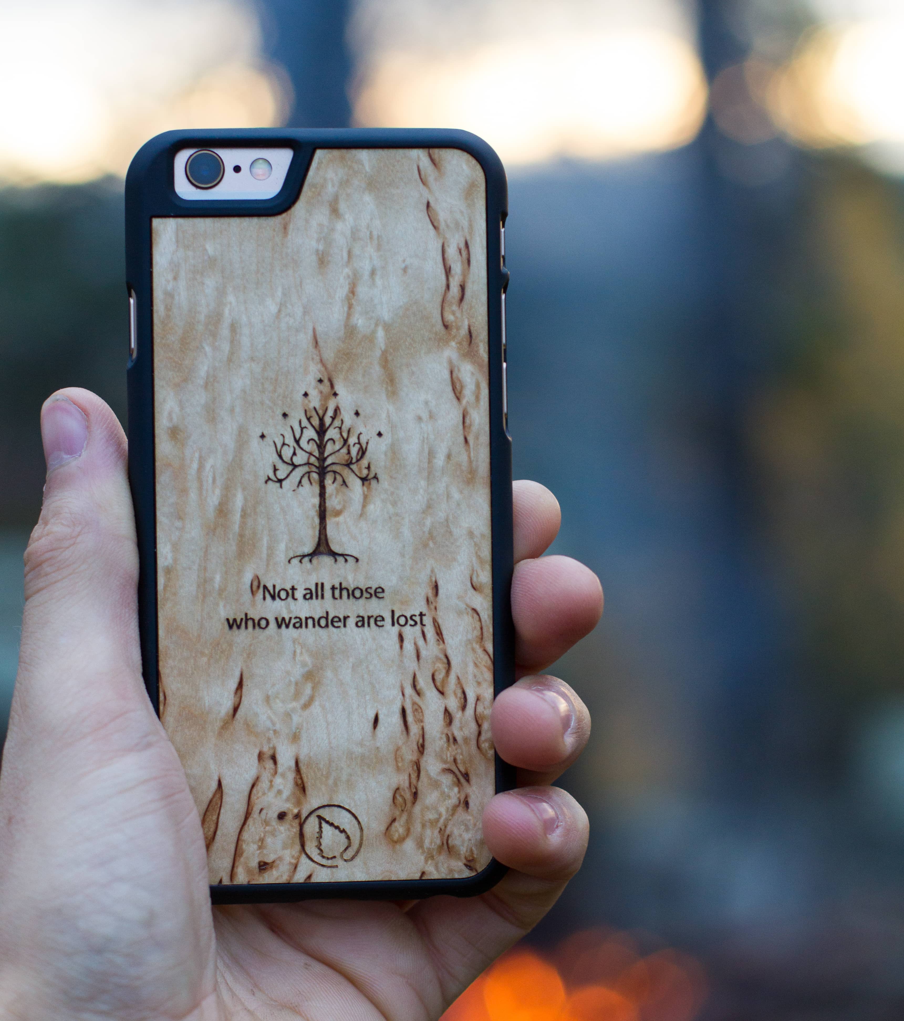 Lastu Käsi pitää iPhone 17 Pro -puhelinta puisen Lastu-suojakotelon sisällä, johon on kaiverrettu puukuva ja lainaus.
