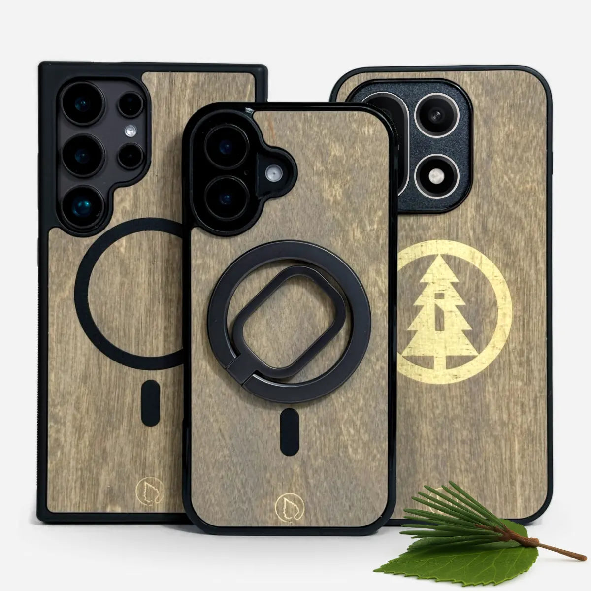 Kolme puhelinkuorta koivupuupinnalla, keskellä MagSafe-yhteensopiva sormirengas ja kaiverrettu kuusikuvio yhdellä kuorella.